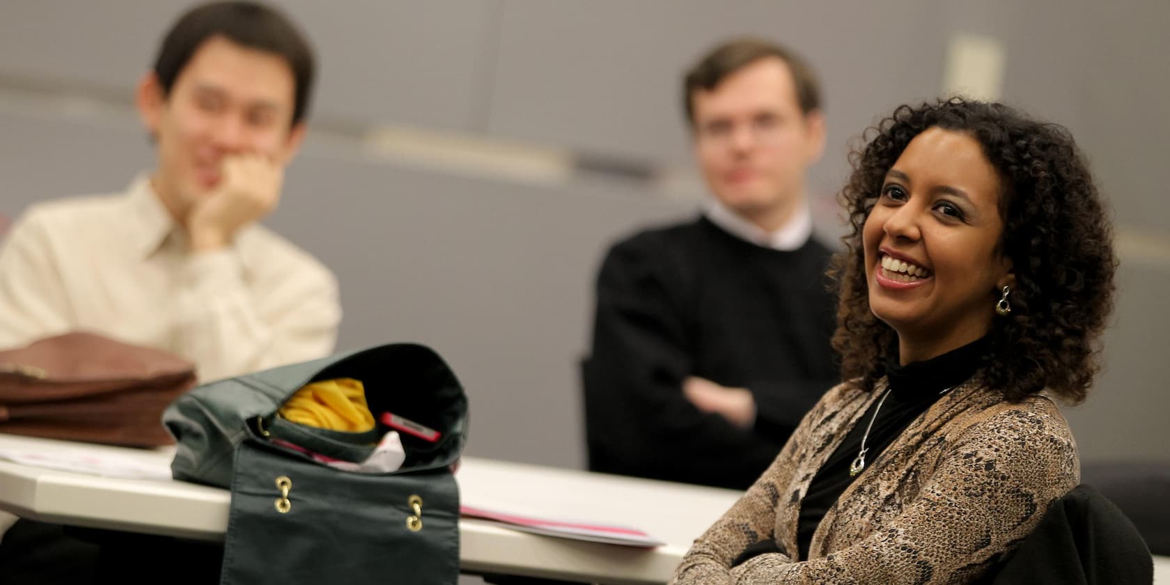 Three people sitting at a table in a meeting room, smiling.