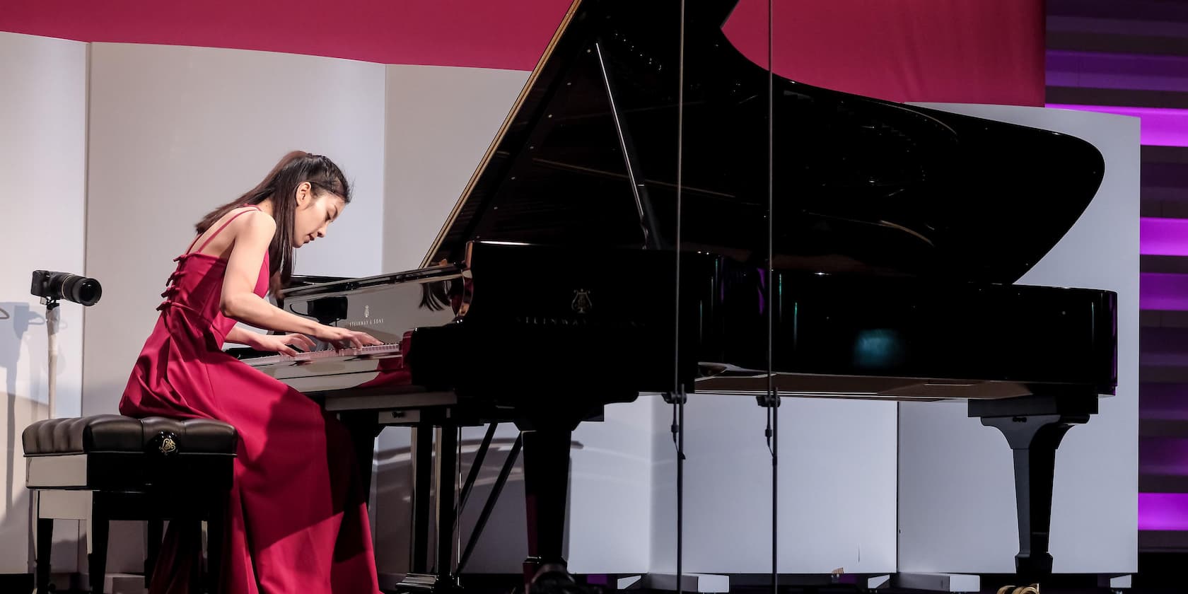 A woman in a red dress playing piano on stage.