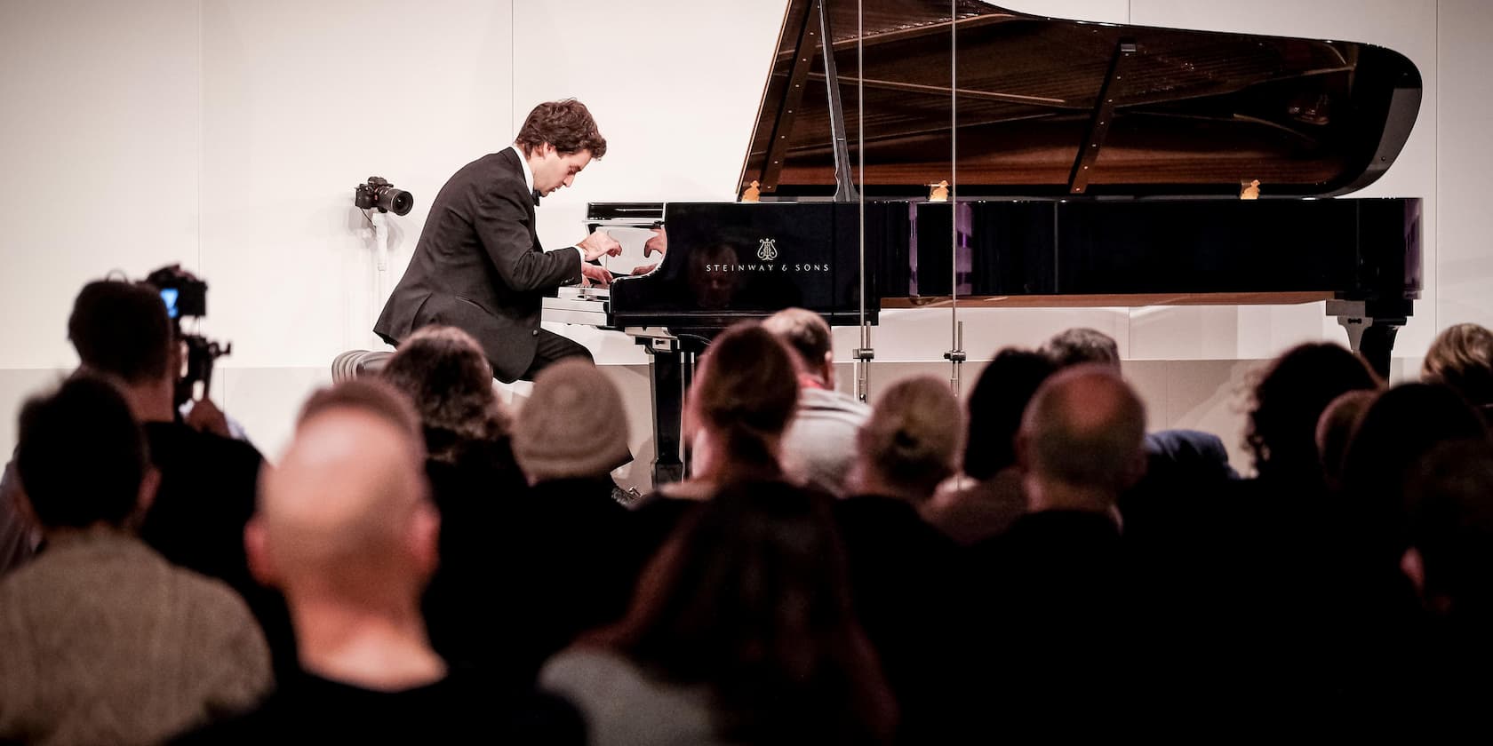 A musician playing the piano at a concert, audience seated in front.