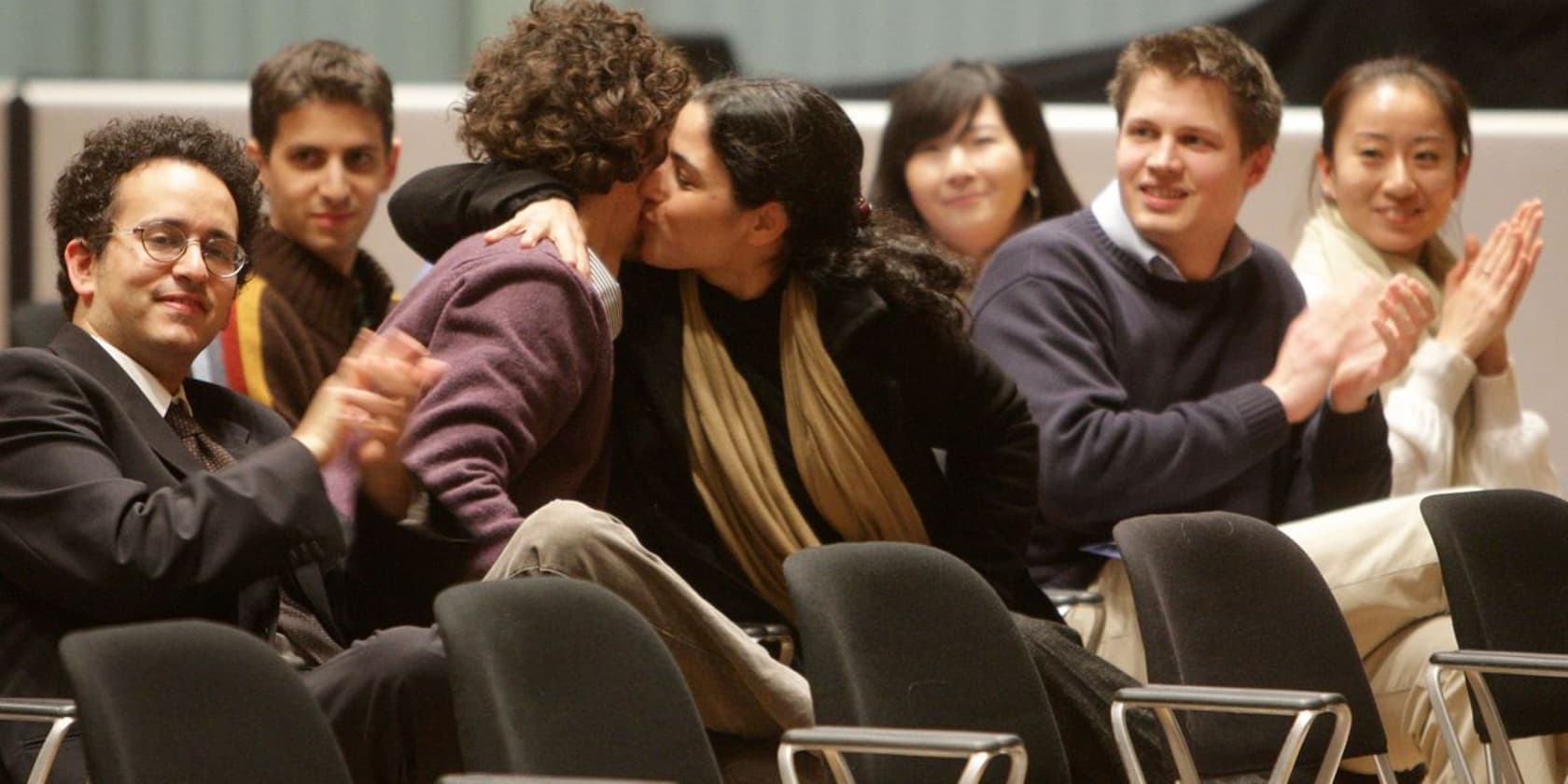 A group of people clapping while two people in the middle are kissing.