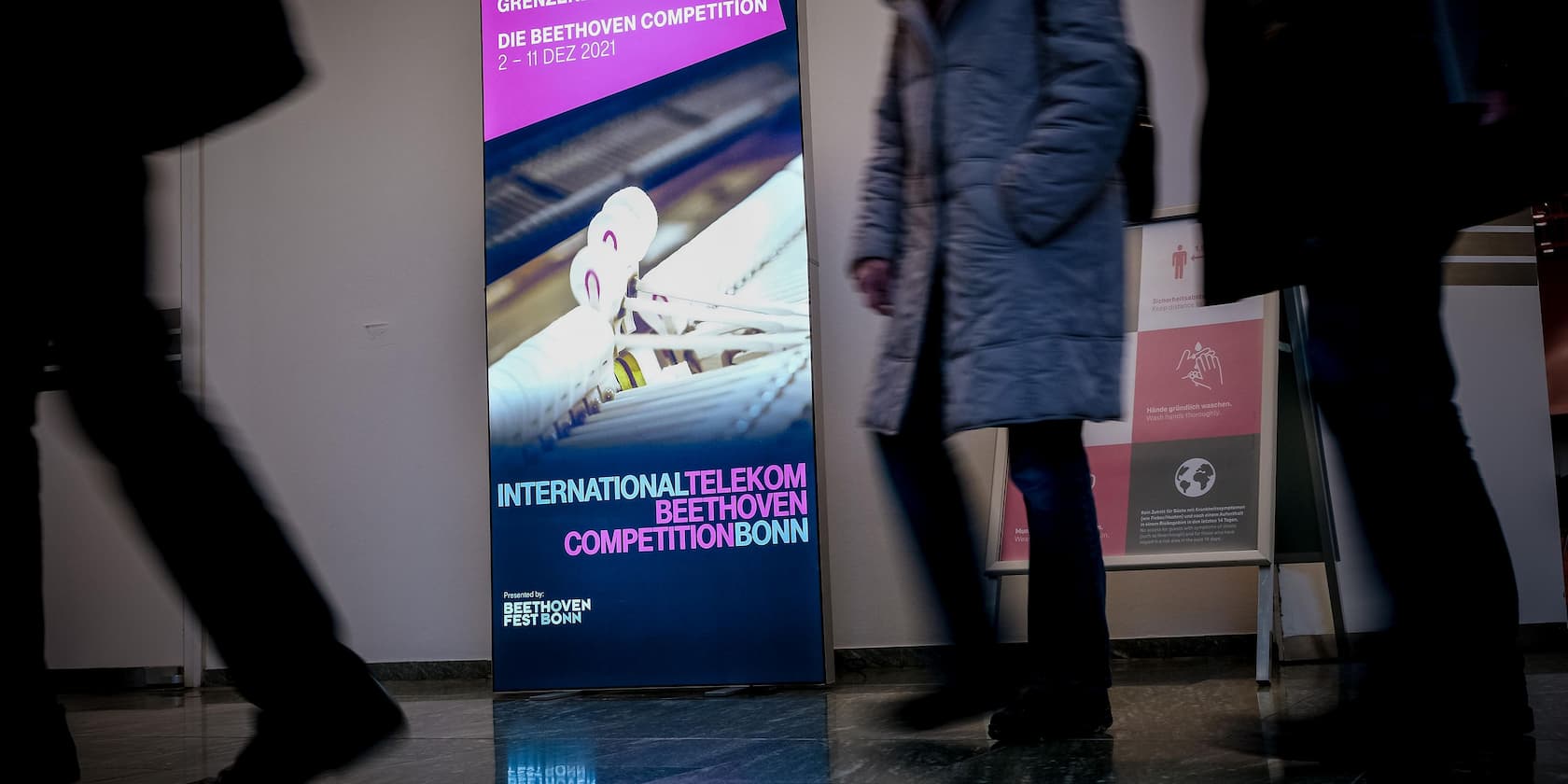 Plakat der International Telekom Beethoven Competition Bonn von 2. bis 11. Dezember 2021. Zwei Personen gehen daran vorbei.