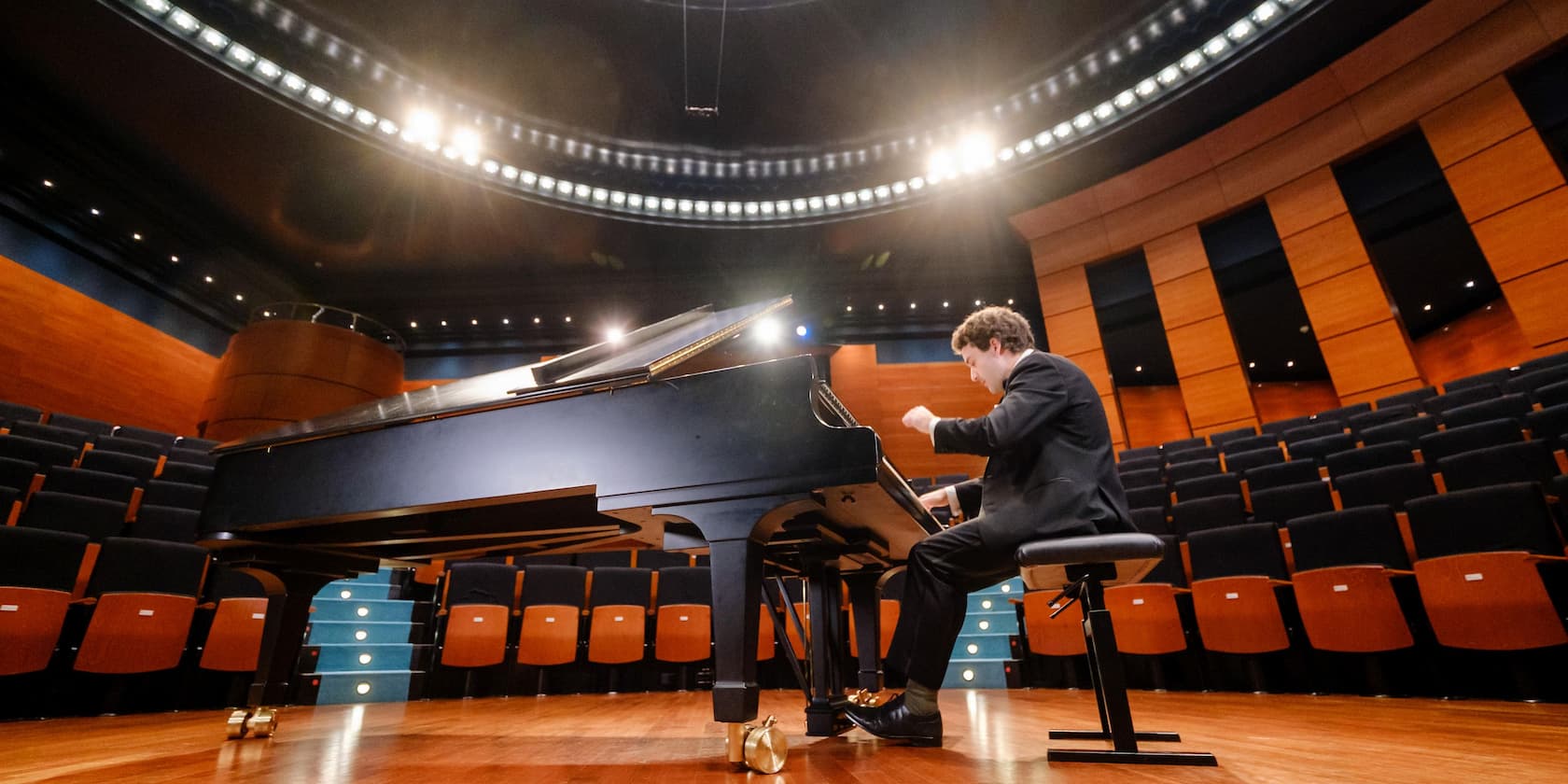 A pianist performs on stage in an empty concert hall.