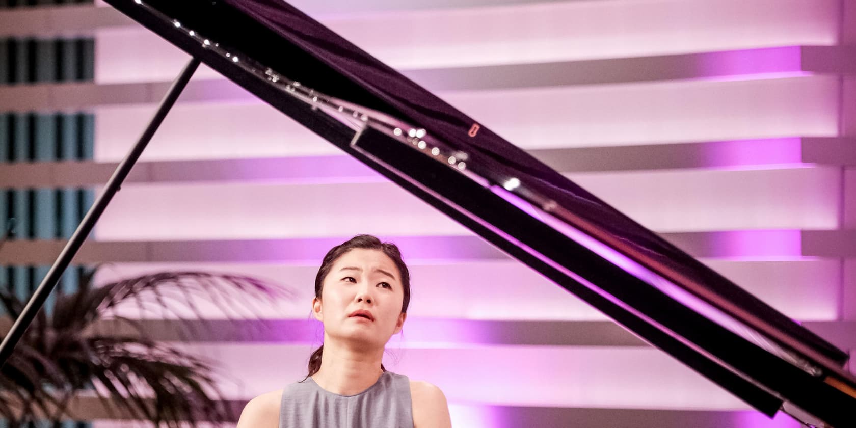 Woman playing the piano in a room with purple-lit walls.