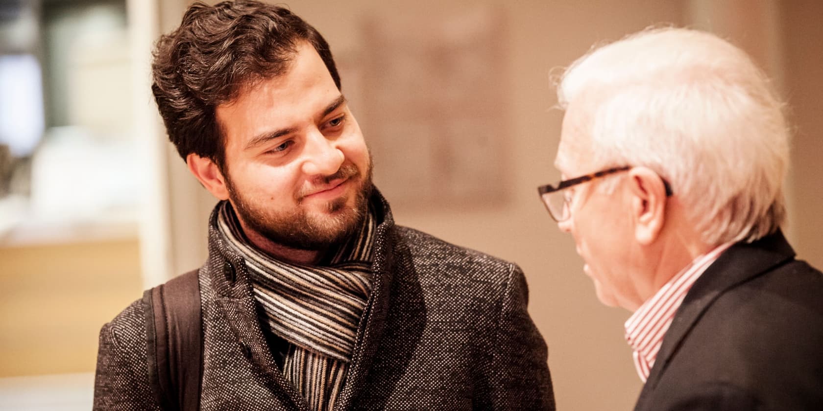 A young man is talking to an older man in a well-lit indoor space.