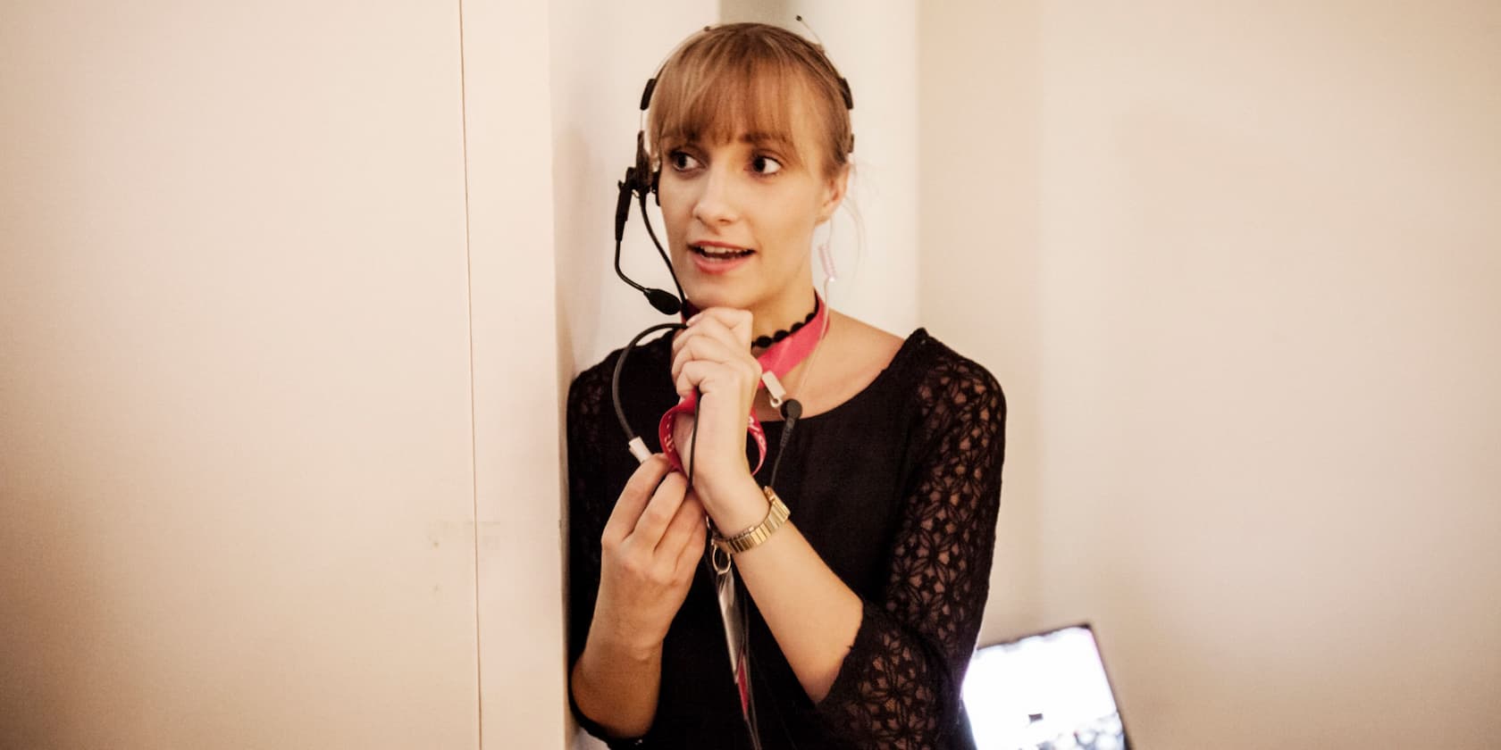 A woman with a headset and microphone speaks next to a wall.