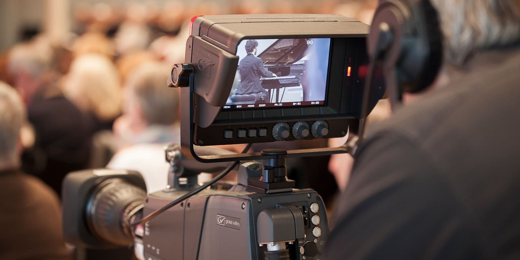 Camera shows a person playing a piano while people are seated in the audience.