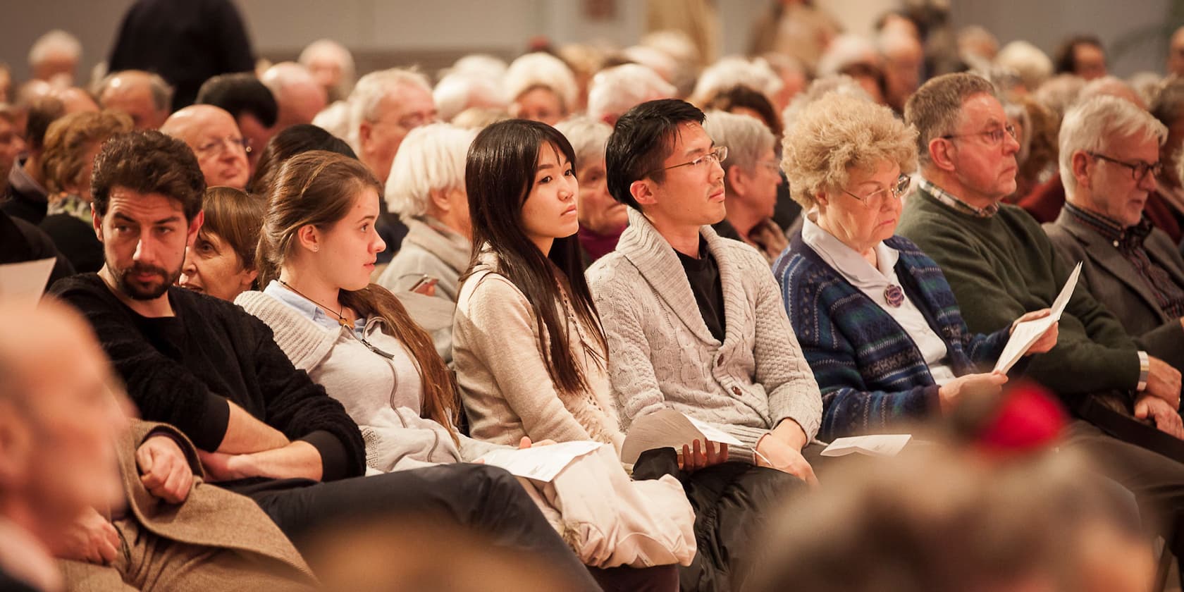 Mehrere Menschen sitzen nebeneinander in einem Auditorium und schauen nach vorne.