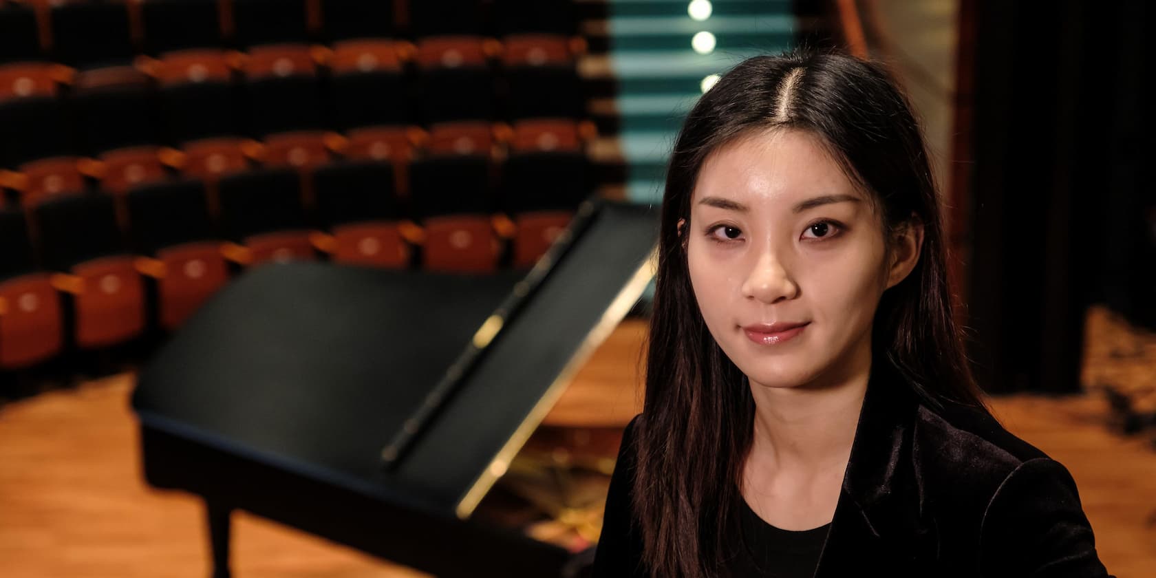 Portrait of a woman in front of a grand piano in an empty concert hall.