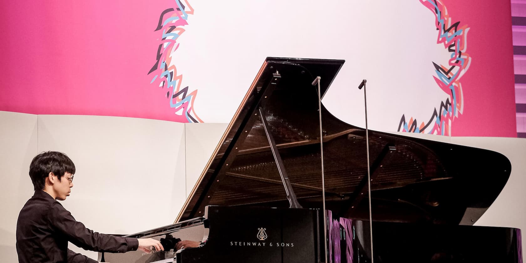 Pianist playing a Steinway & Sons grand piano against a pink background with abstract artwork.