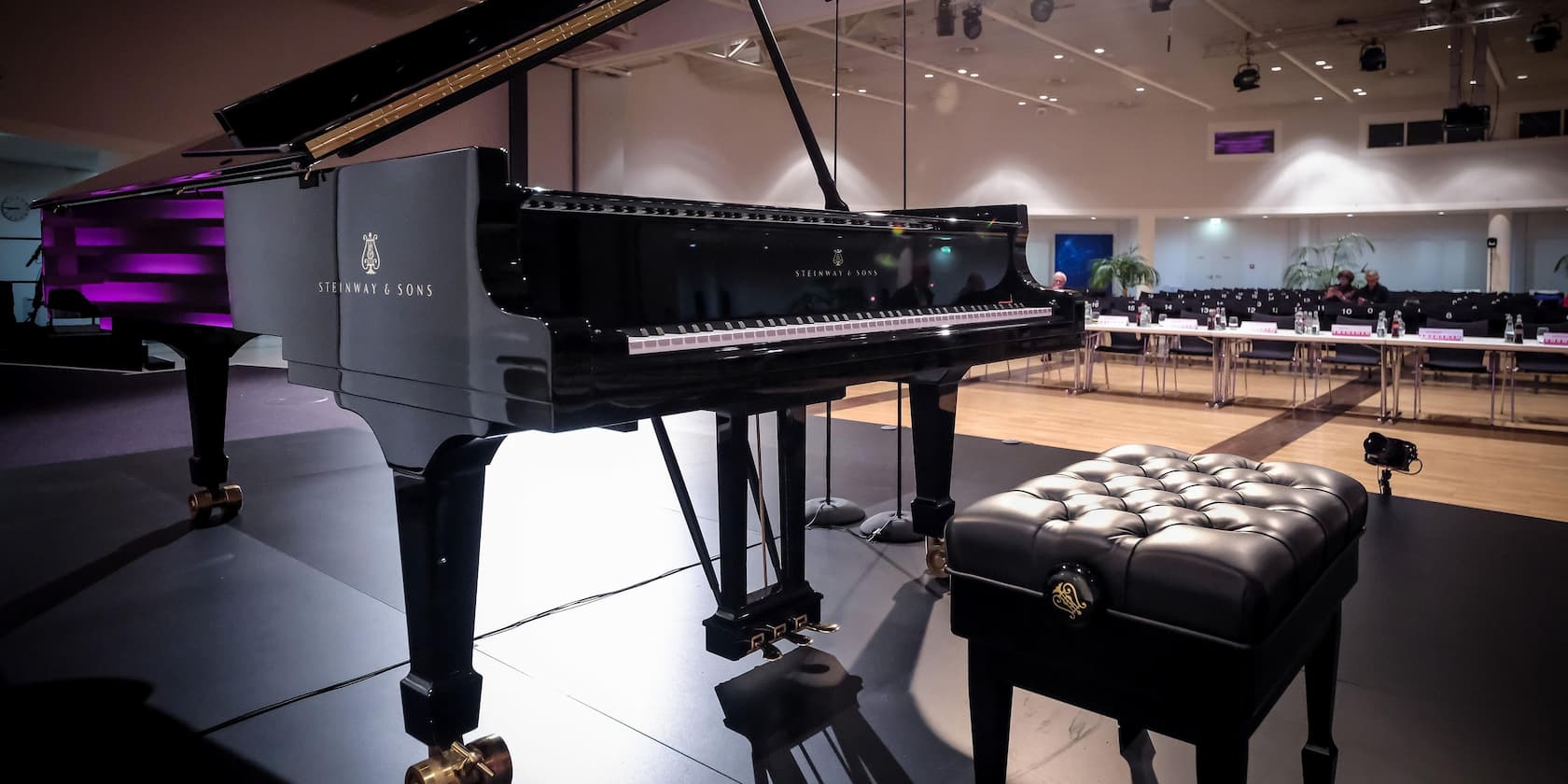 Black Steinway & Sons grand piano on a stage with a cushioned piano bench in the foreground.