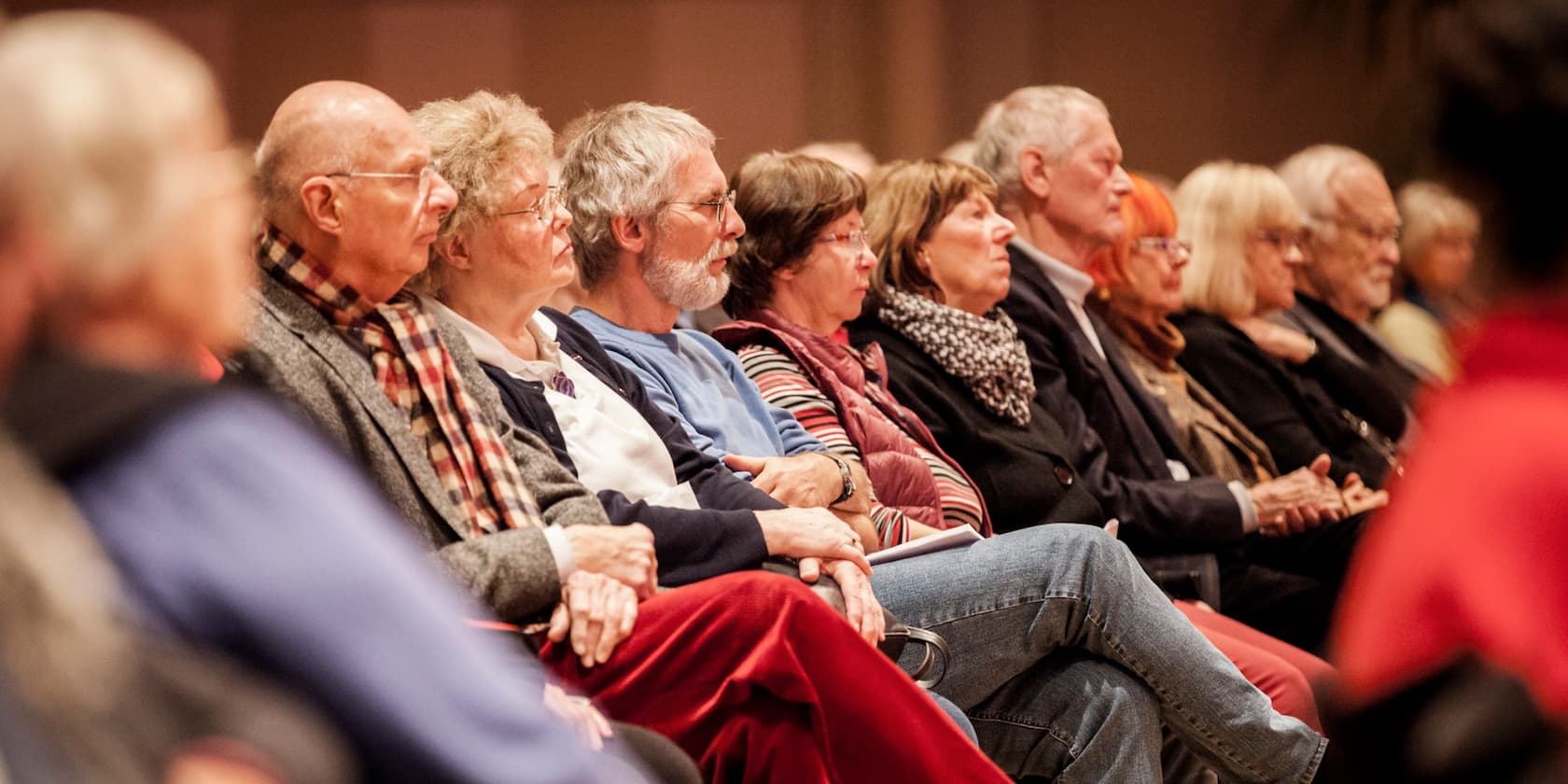 A group of elderly people sitting in a row and listening attentively.