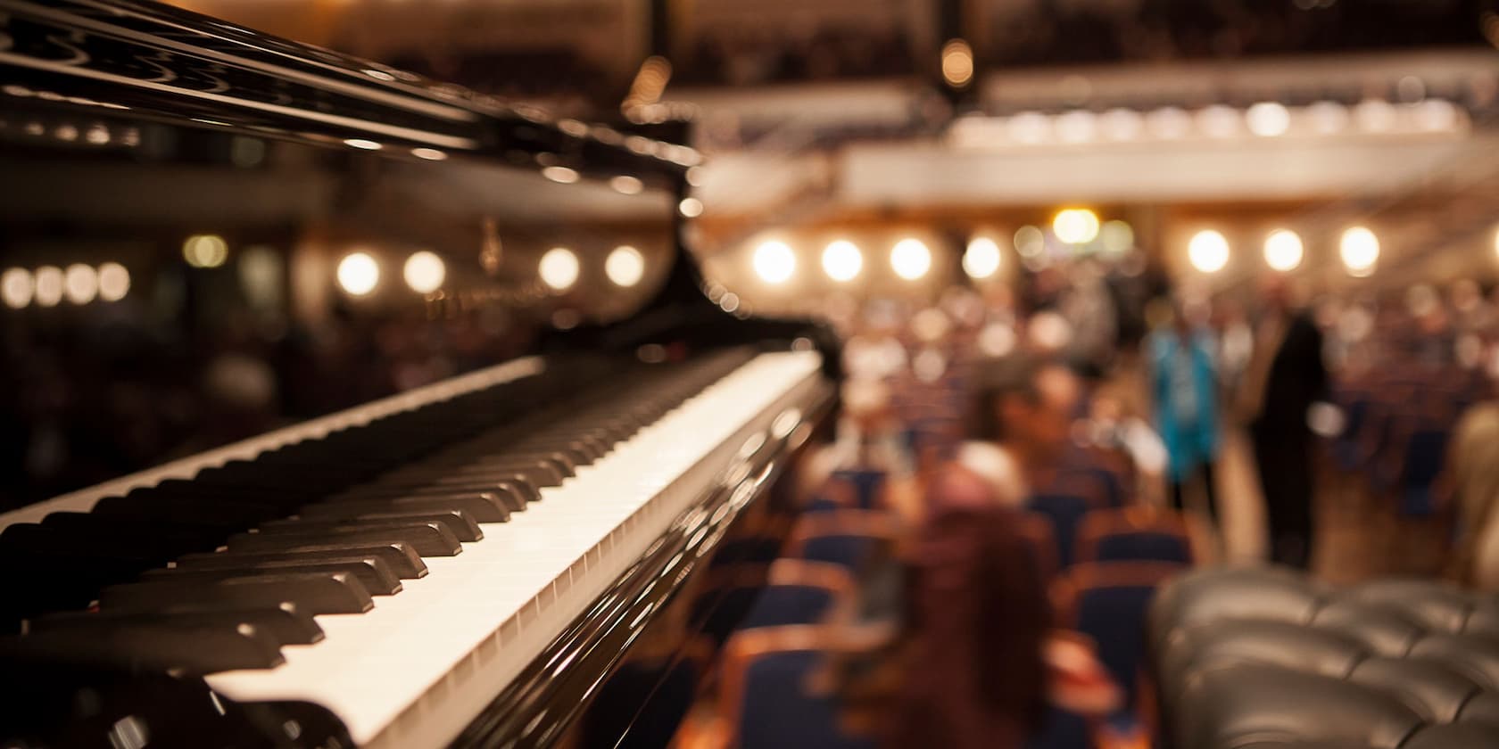 Piano in the foreground with a blurred audience in the background in a concert hall