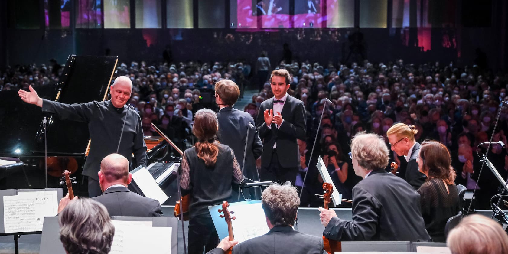 An orchestra in front of a large audience, a conductor is bowing.