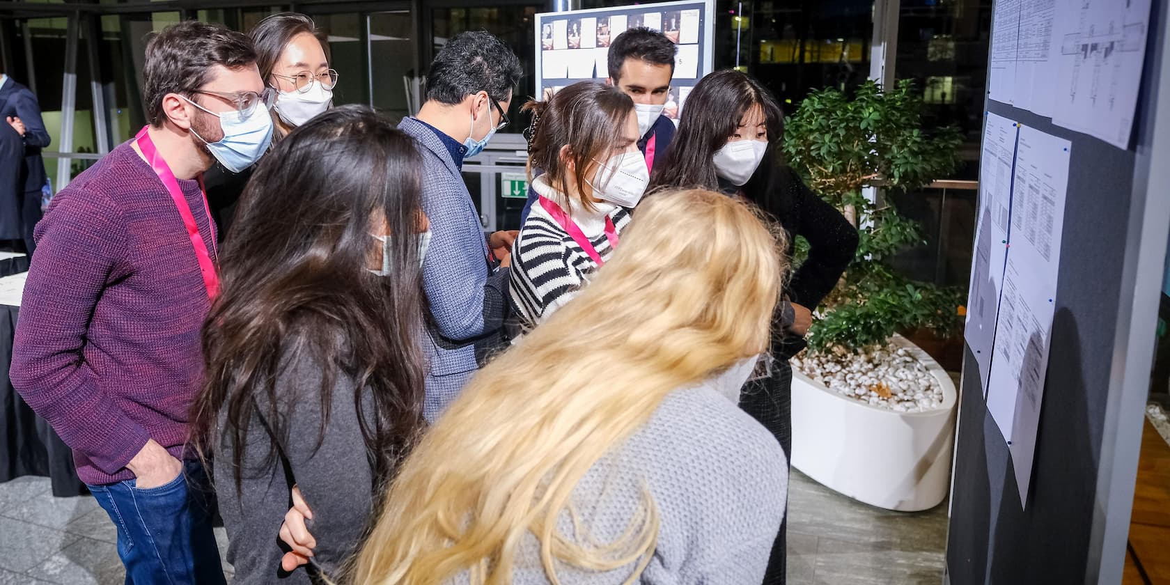 A group of people wearing masks look at a wall with documents.