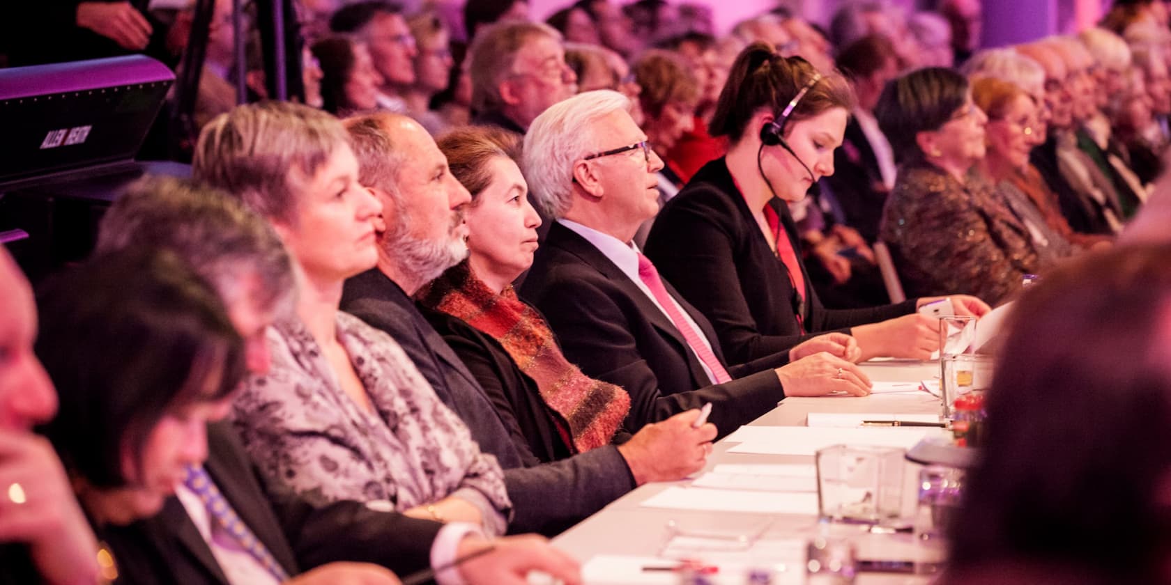 People sitting at a table attentively listening, with a man wearing a headset