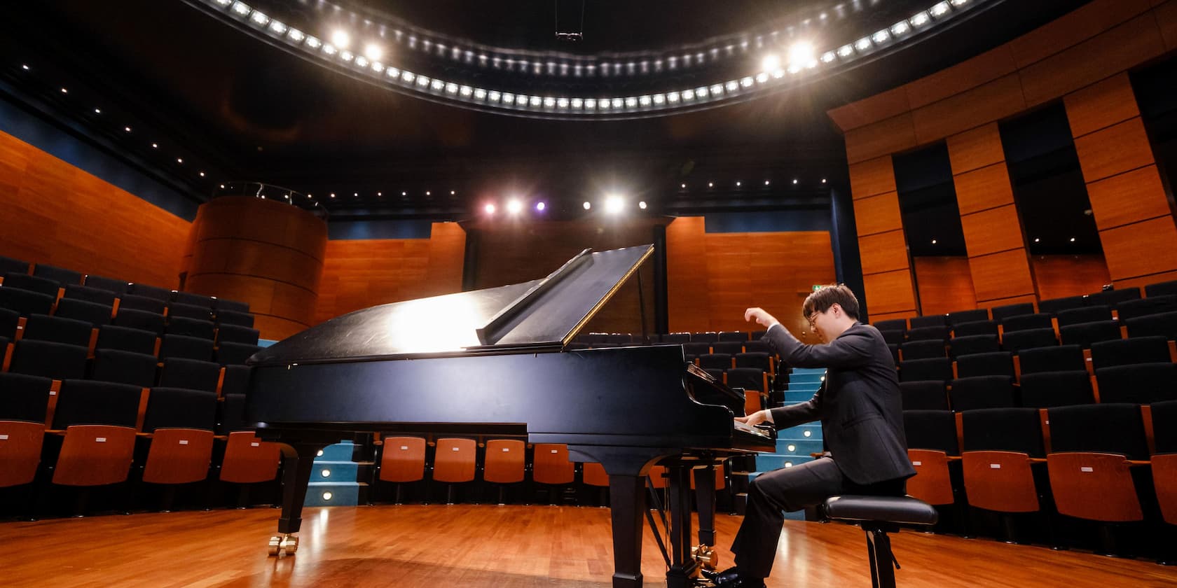 A man playing the piano in an empty concert hall.