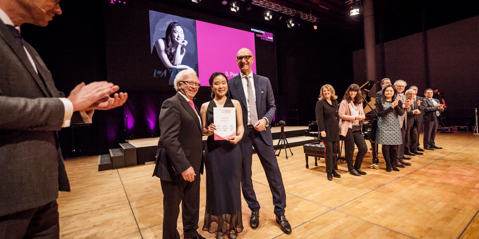 People on a stage clapping as a woman holds a certificate