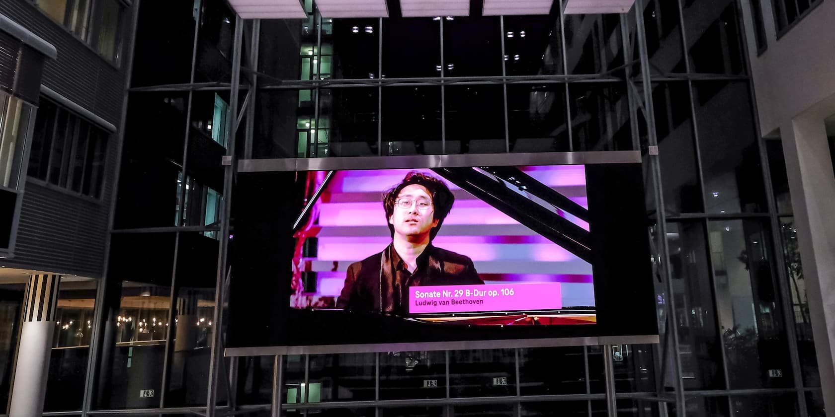 A large advertisement display in a building shows a person with a piano. The text on the display reads 'Sonata No. 29 in B-flat major op. 106 Ludwig van Beethoven'.