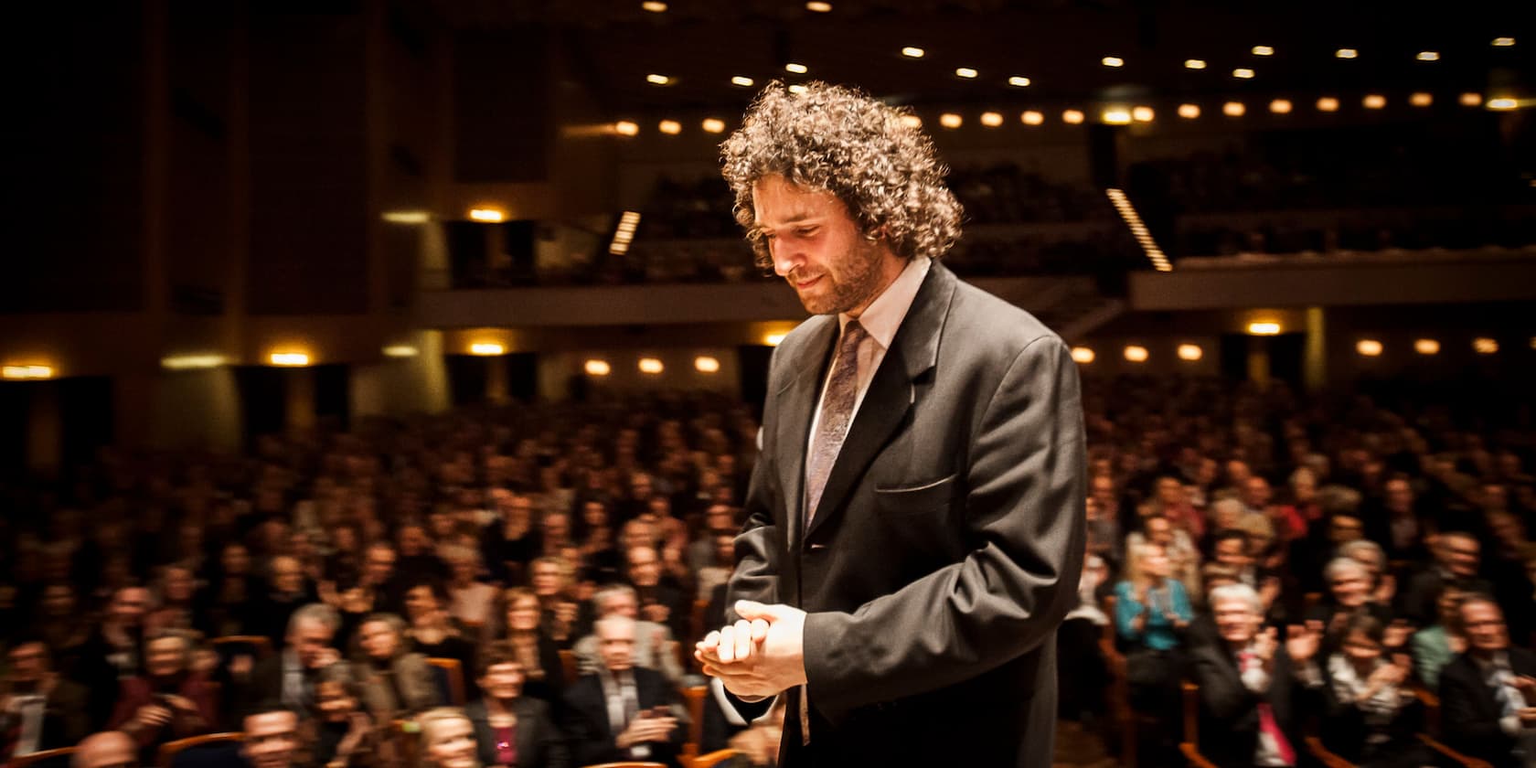 A man in a suit bows in front of an audience in a well-lit auditorium.