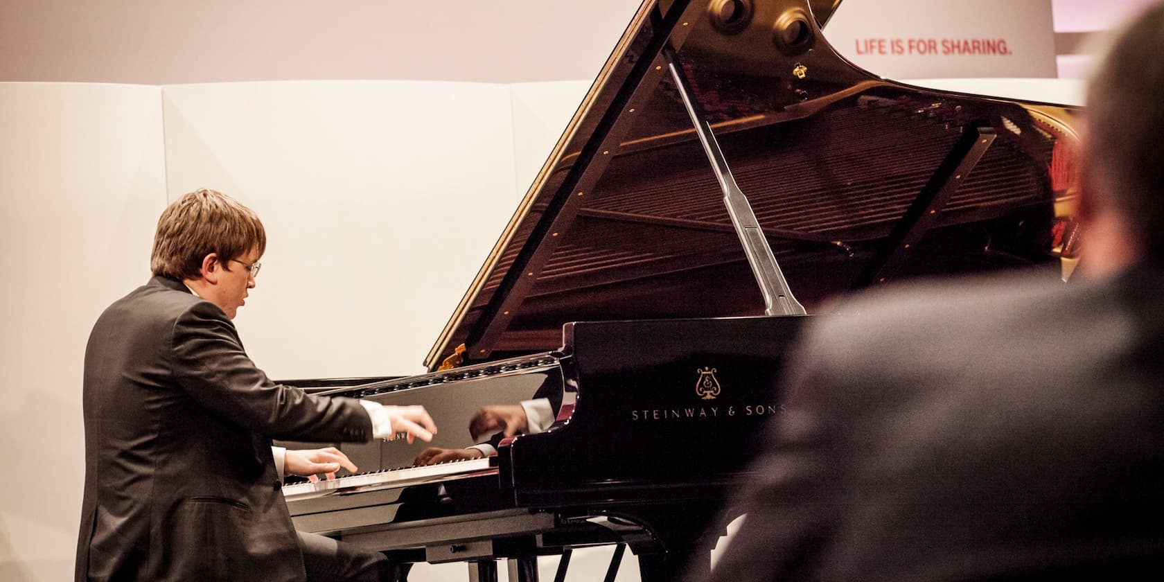 A man playing a Steinway & Sons piano with the text 'Life is for sharing' in the background.