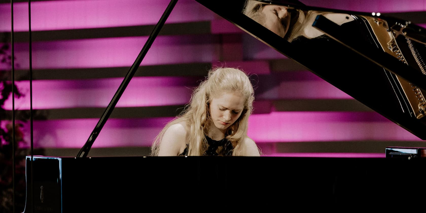 Woman playing piano at a concert with a violet-lit background.