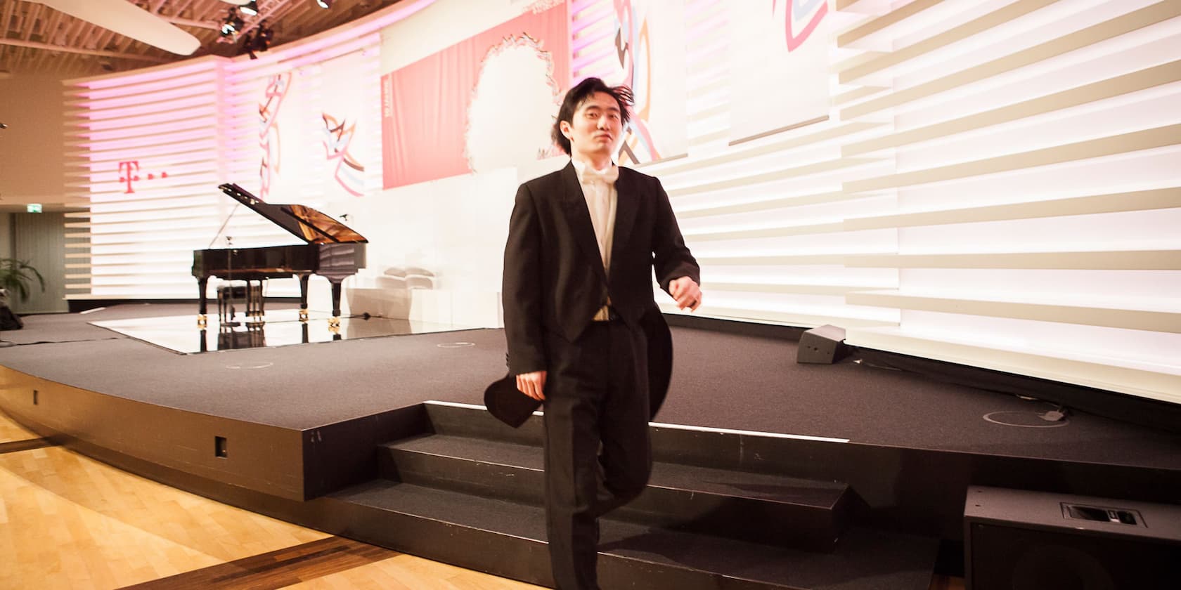 A pianist in formal attire leaves the stage after a performance, with a grand piano in the background.