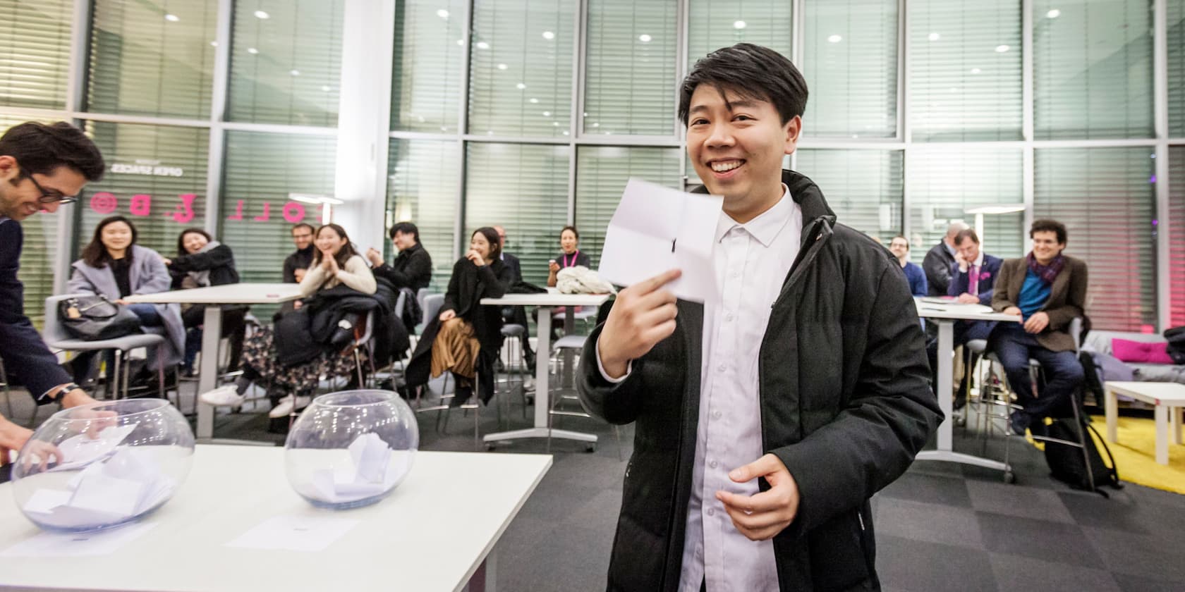 A man holds a piece of paper while a group of people claps in the background.