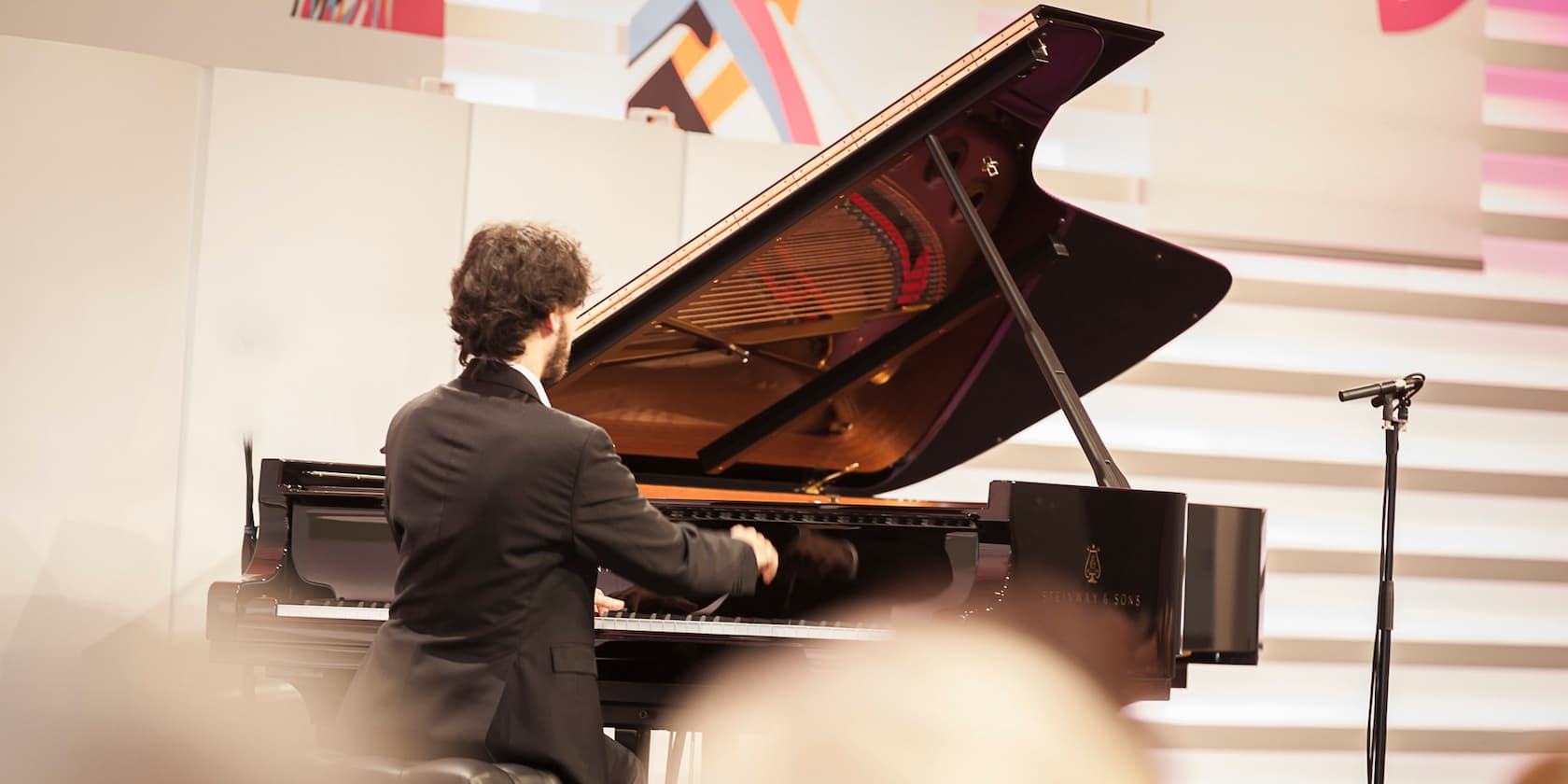 Man in a suit playing a grand piano on a stage.