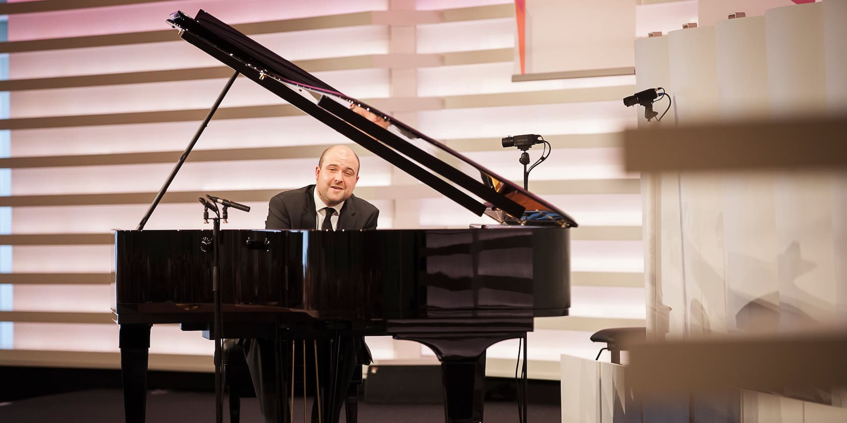 A man in a suit sits at a grand piano playing.