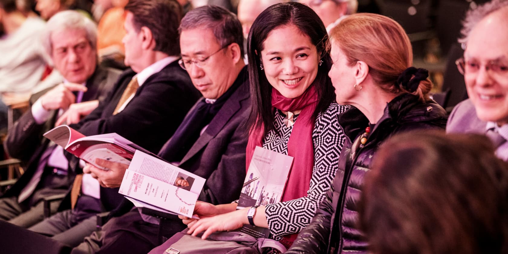 People sitting next to each other and talking at an event. Some are holding books in their hands.