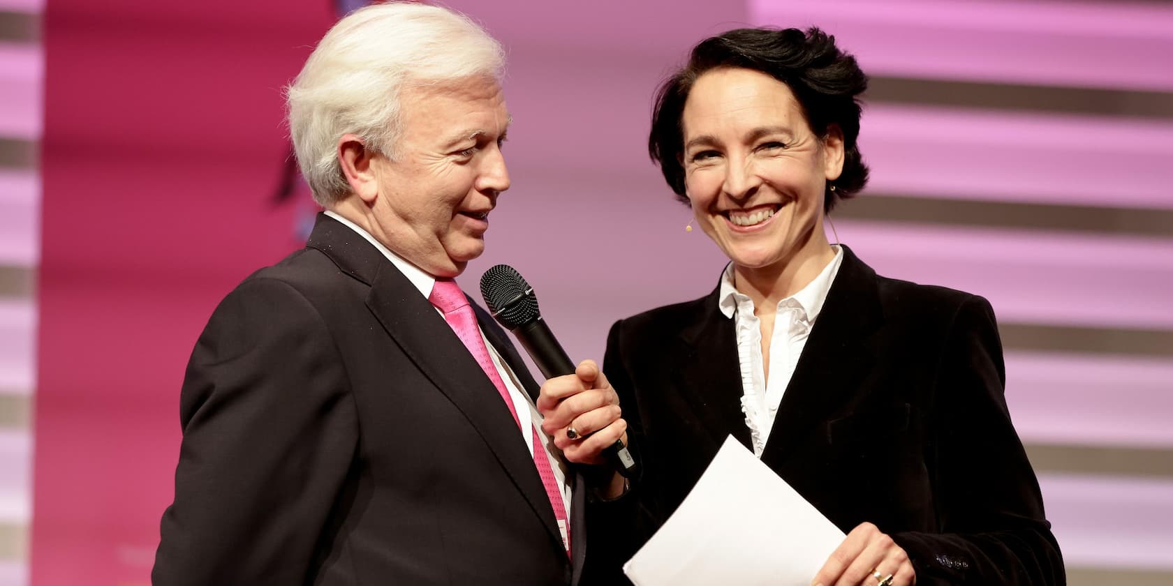 A man and a woman are having a conversation at an event. The man is holding a microphone.