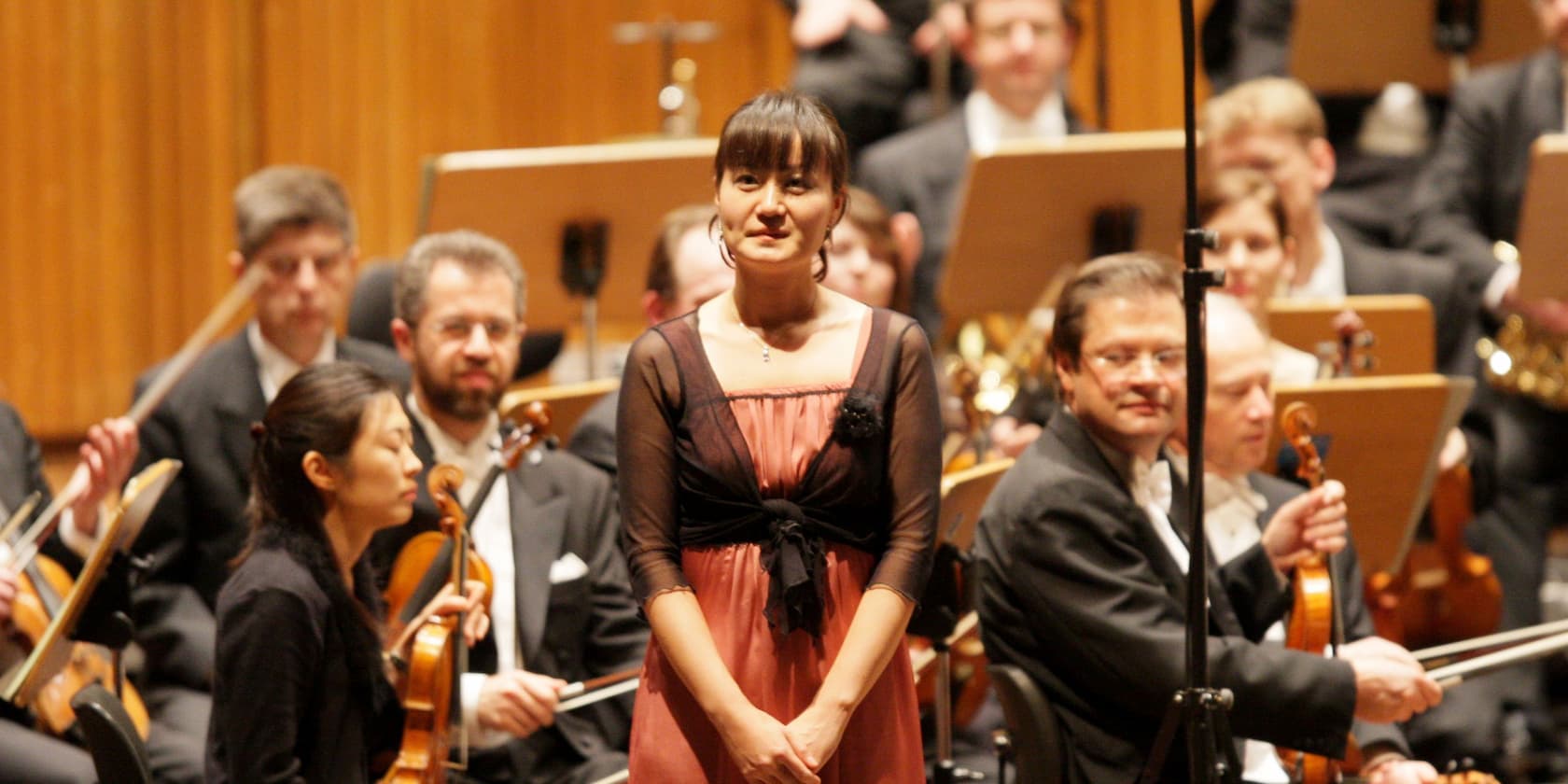 Eine Frau steht auf der Bühne vor einem Orchester.