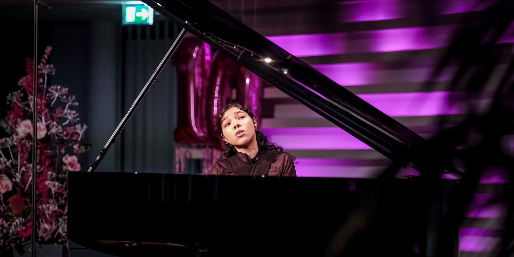 A woman playing piano on a stage with purple lighting.