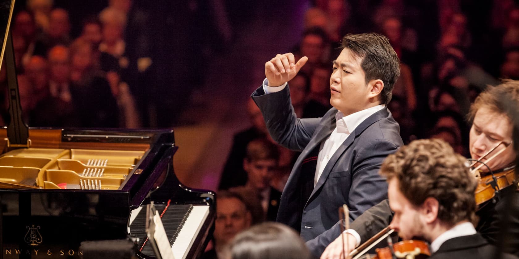 A pianist plays the piano during a concert, surrounded by an orchestra.