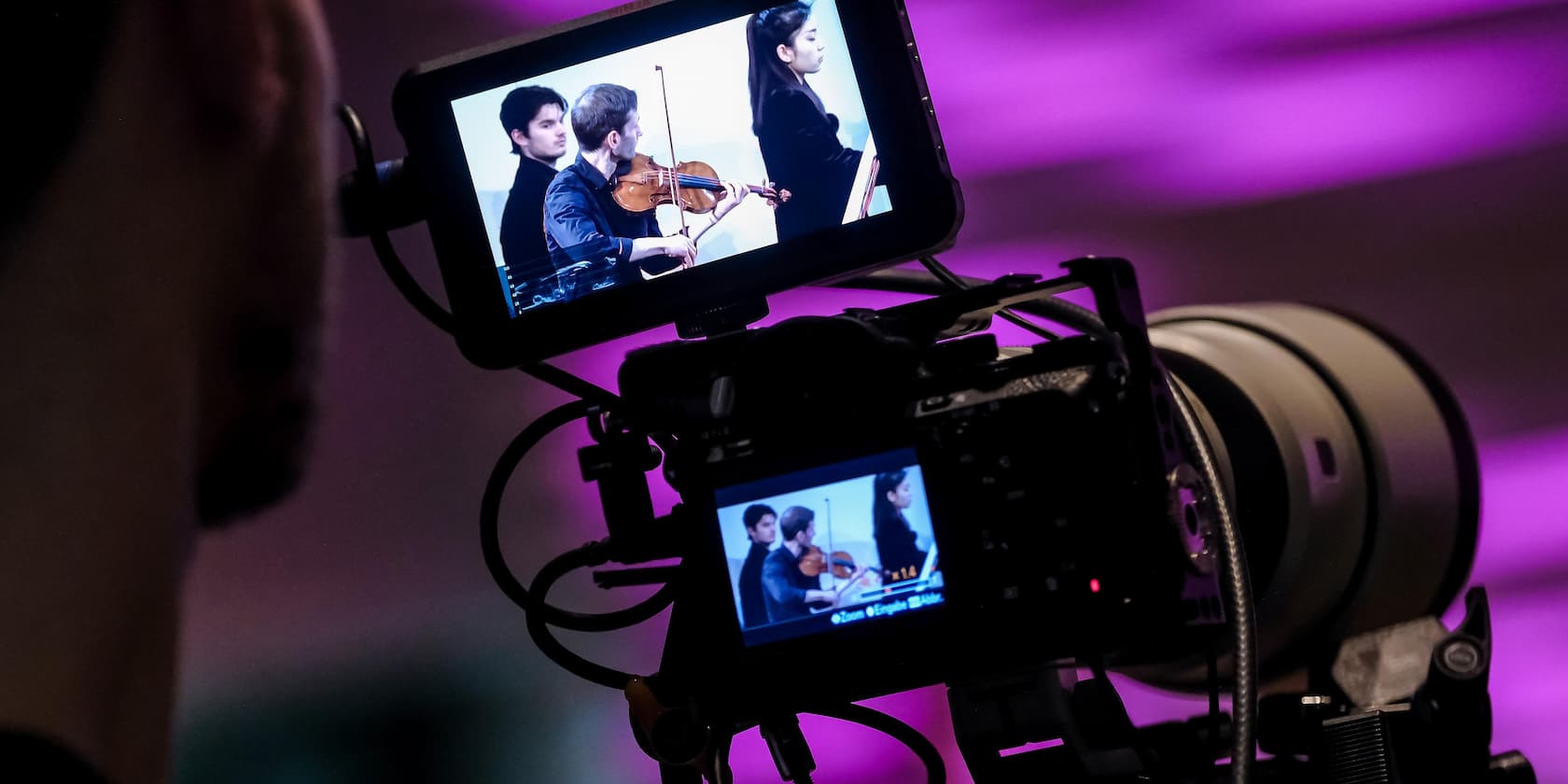 Camera setup capturing an orchestra with a violinist on a screen.