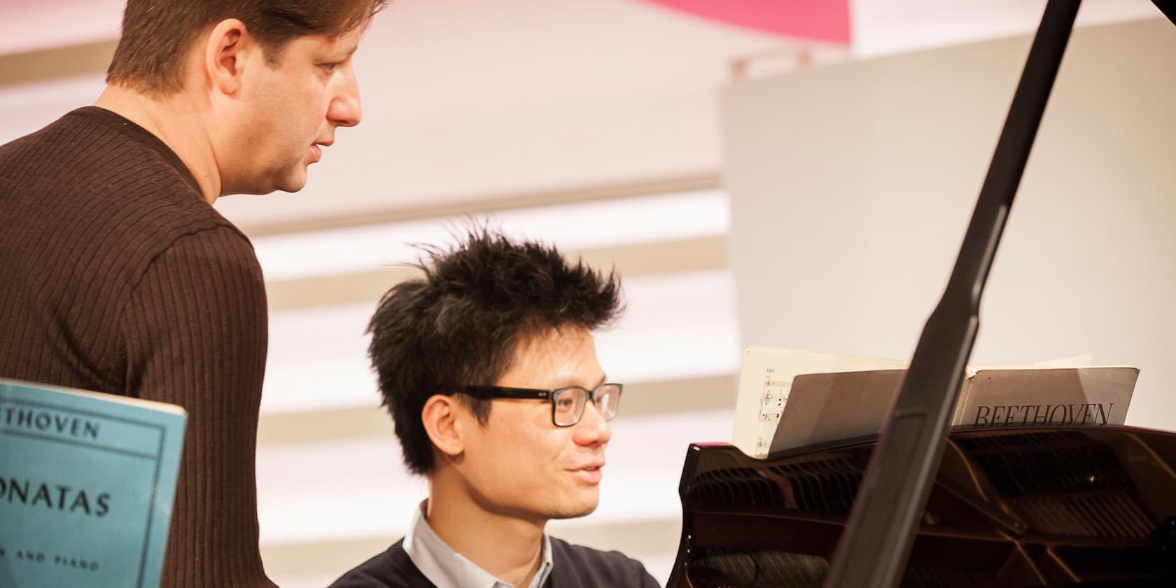 A man and a student sit at a piano looking at sheet music.