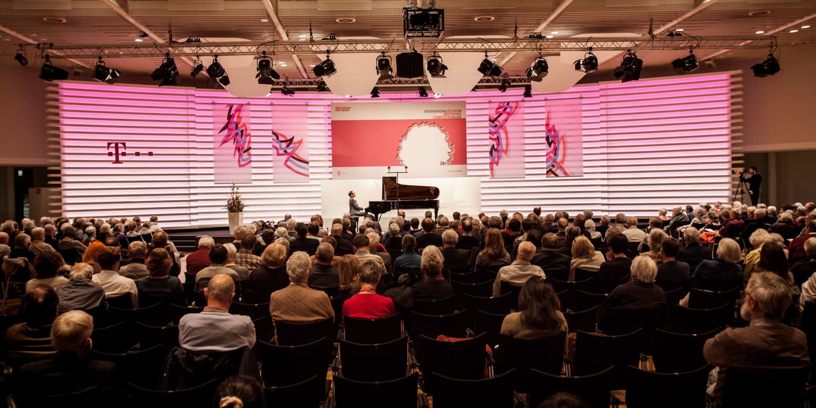 A man plays the piano on a stage at an event, while the audience watches.