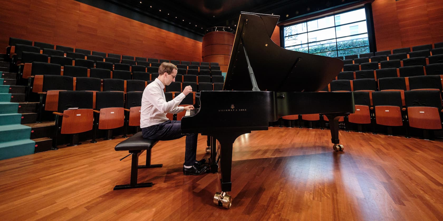 A man plays the piano in an empty concert hall.