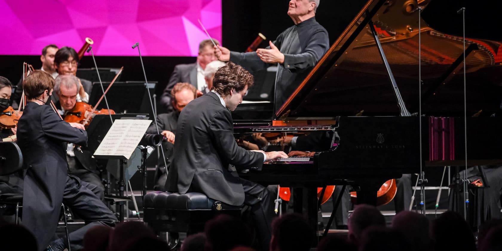 A pianist performs with an orchestra on stage under the direction of a conductor.