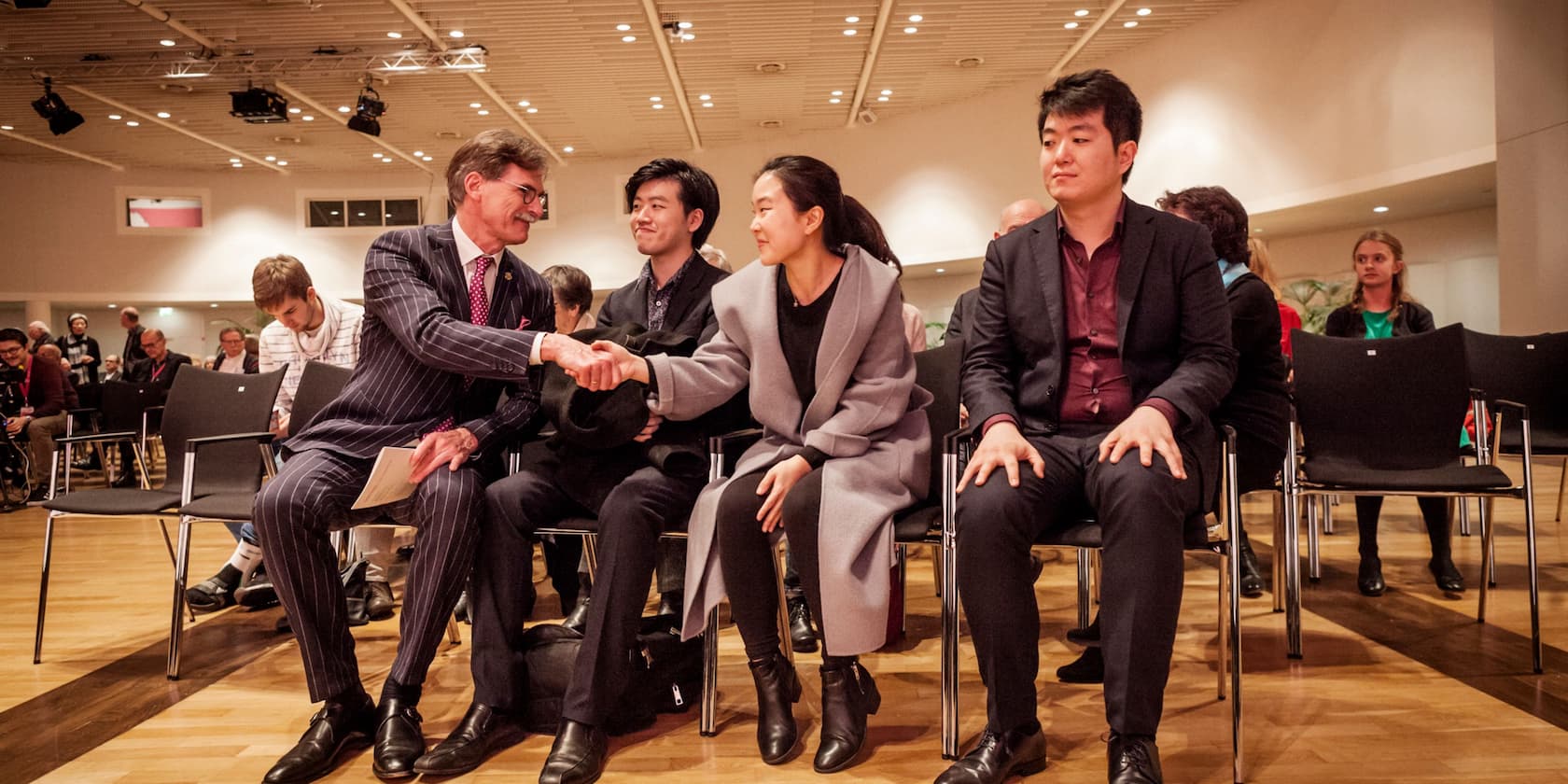 A man and a woman shaking hands in a conference room, while two other people sit beside them.