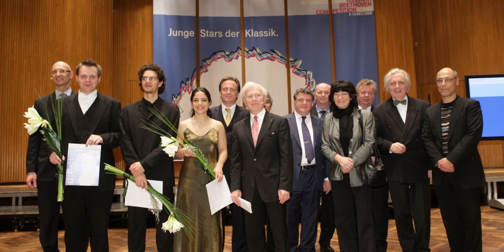 Gruppenfoto von Teilnehmern und Veranstaltern des Klassik-Wettbewerbs 'Junge Stars der Klassik' in einem Konzertsaal.