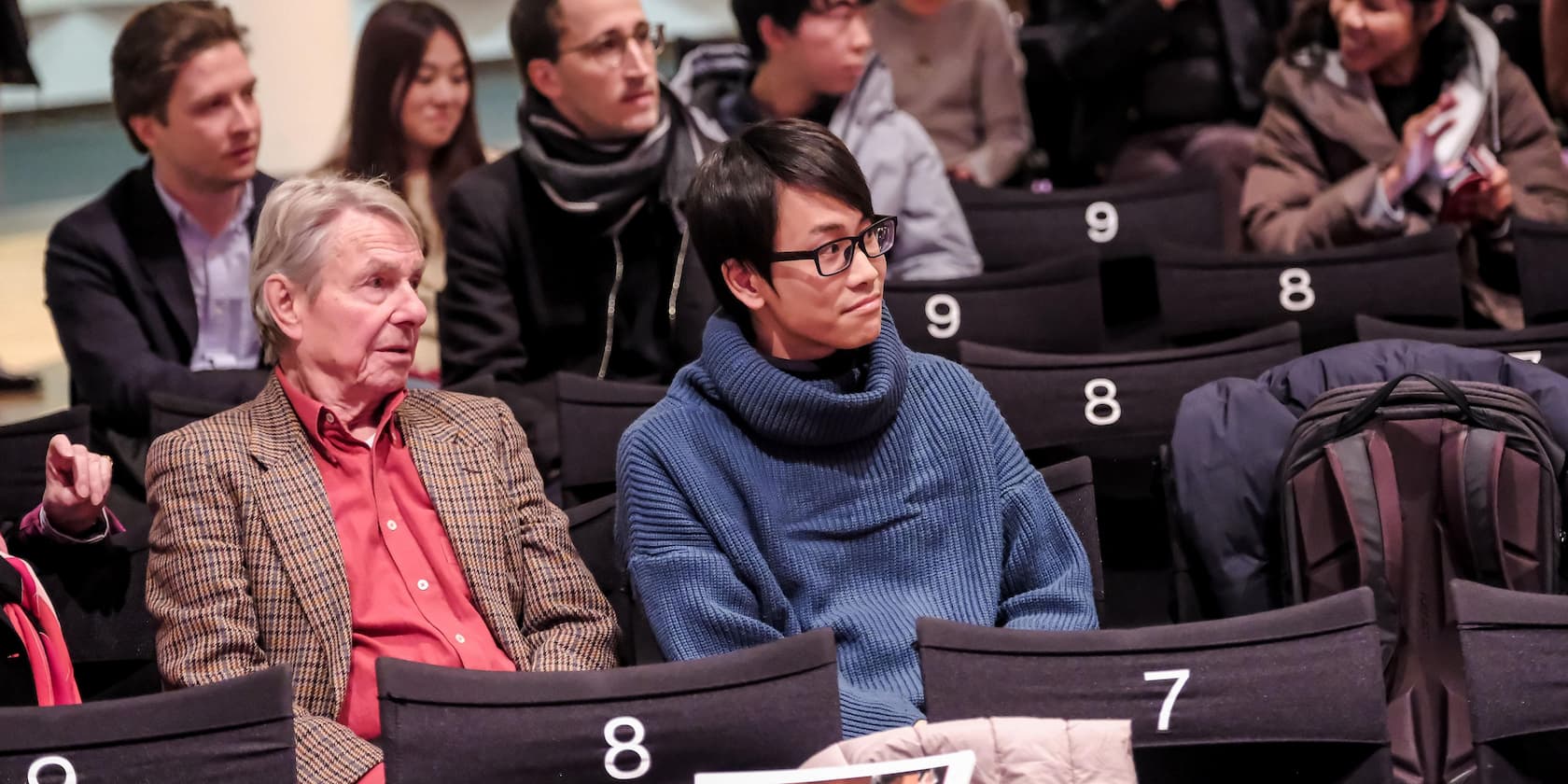 Audience members seated in numbered seats in an auditorium.