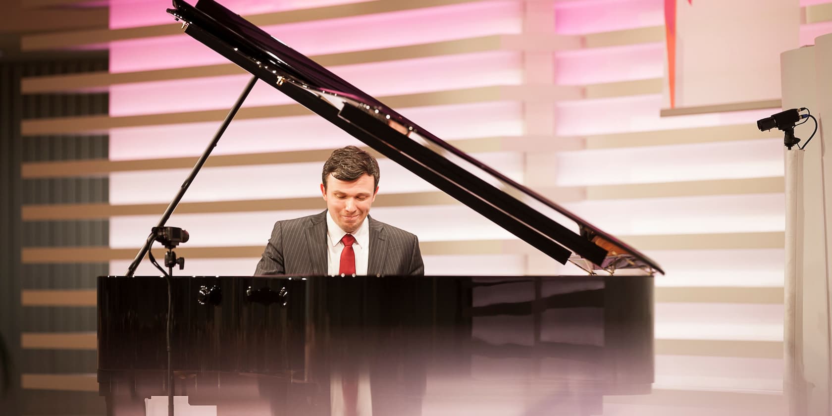 A man in a suit plays piano in a modern lit room.