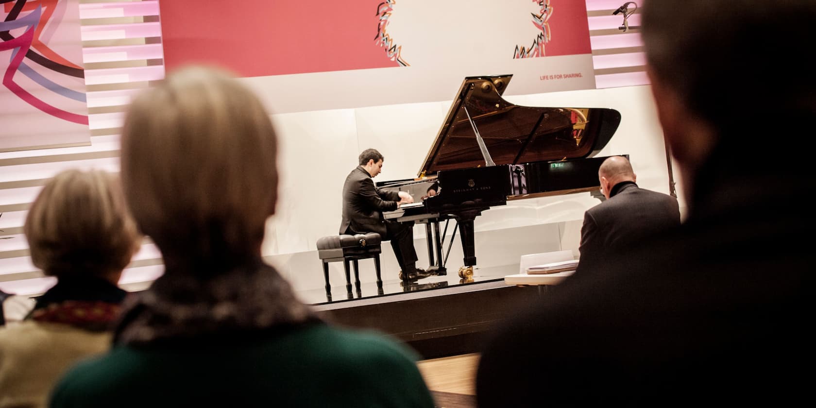 Ein Pianist spielt auf einer Bühne vor einem Publikum.