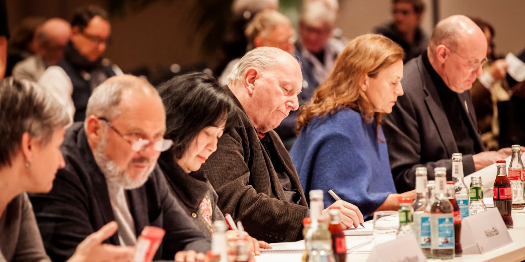 Menschen sitzen an einem Tisch und schreiben auf Notizblöcke während einer Besprechung.