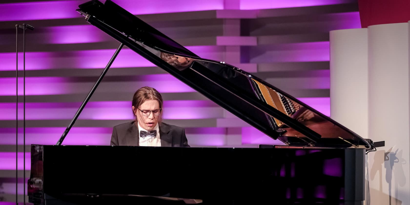 Person playing piano with purple background lighting.