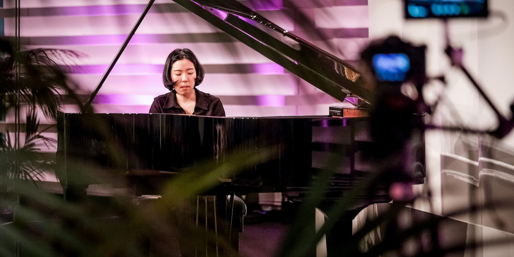 Woman playing a piano during a performance with purple lighting.