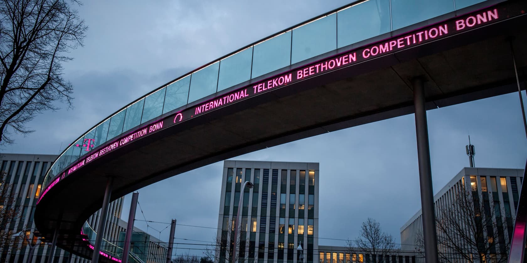 Pedestrian bridge with the sign 'International Telekom Beethoven Competition Bonn' in pink neon lights.