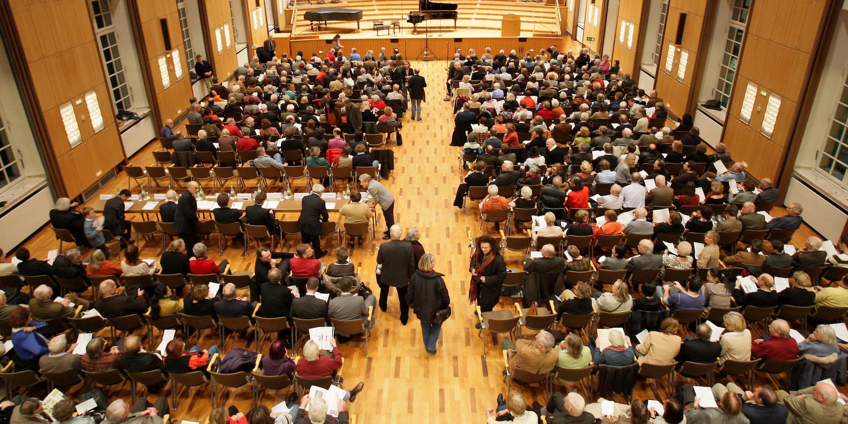 Menschenmenge in einem großen Saal, der auf eine Bühne ausgerichtet ist.