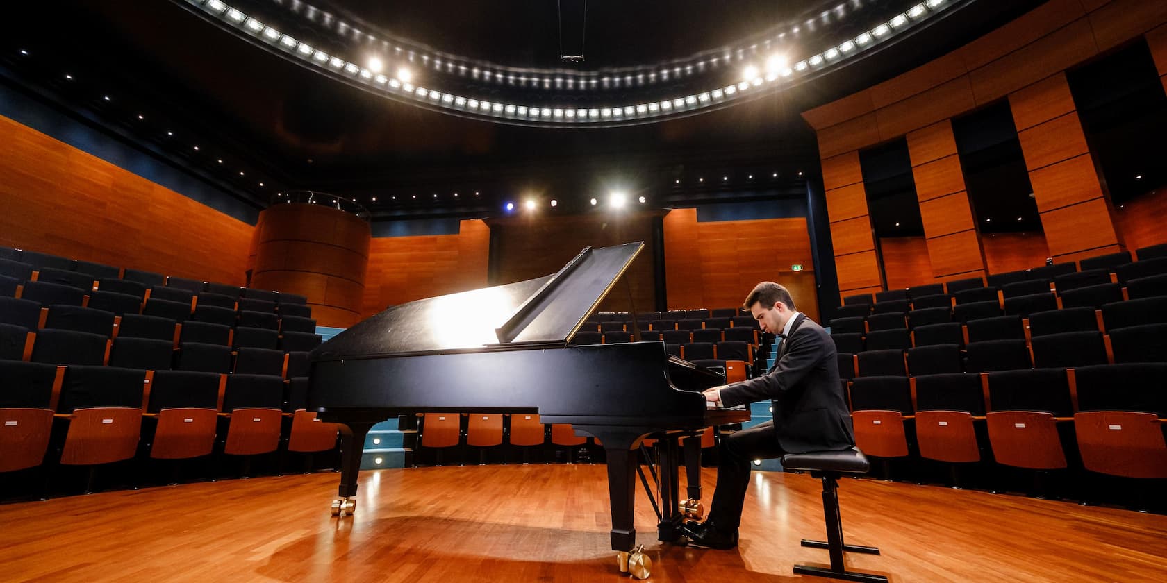 A man is playing piano in an empty concert hall.